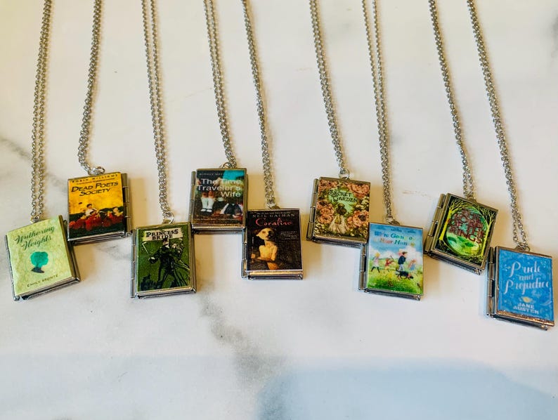May include: A selection of miniature book pendant necklaces. Each pendant displays a different book cover design, with titles such as "Pride and Prejudice" and "Wuthering Heights." The pendants are suspended from silver-coloured chain necklaces.