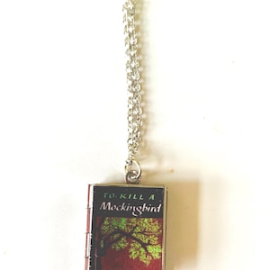 May include: A silver-colored chain necklace with a miniature book pendant. The book cover features the title "To Kill a Mockingbird" with a tree illustration and the author's name, Harper Lee, on a red background.