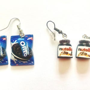 K&ouml;nnte beinhalten: Ohrringe mit Miniatur-Lebensmitteln. Ein Paar zeigt Oreo-Keksverpackungen in Blau und Wei&szlig;, mit einem schwarzen Keks. Das andere Paar zeigt kleine Nutella-Gl&auml;ser mit braunen Deckeln und wei&szlig;en Etiketten.