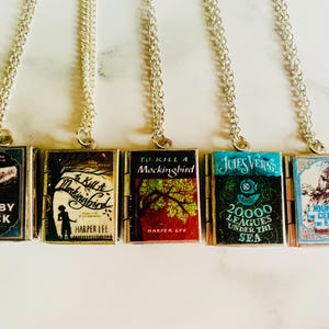 May include: Five silver-toned necklaces, each featuring a miniature book pendant. The book covers display titles like "Moby Dick" and "To Kill a Mockingbird." The pendants are rectangular with detailed cover art and text.