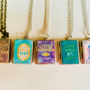May include: Five book-shaped pendant necklaces. The pendants feature book covers from classic novels, including "Adventures of Huckleberry Finn" and "Little Women." Each pendant is attached to a chain. The first chain is dark bronze, and the others are silver.