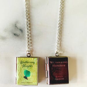 May include: Two silver chain necklaces each feature a small, book-shaped pendant. One pendant is green and yellow with the title "Wuthering Heights" and a silhouette. The other is burgundy with the same title.