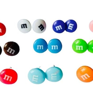 Peut inclure: Un ensemble de 10 paires de boucles d'oreilles clous colorées en forme de bonbons M&M's. Chaque paire présente une couleur différente, notamment le rouge, le bleu, le vert, l'orange, le rose, le blanc, le marron et le bleu clair.
