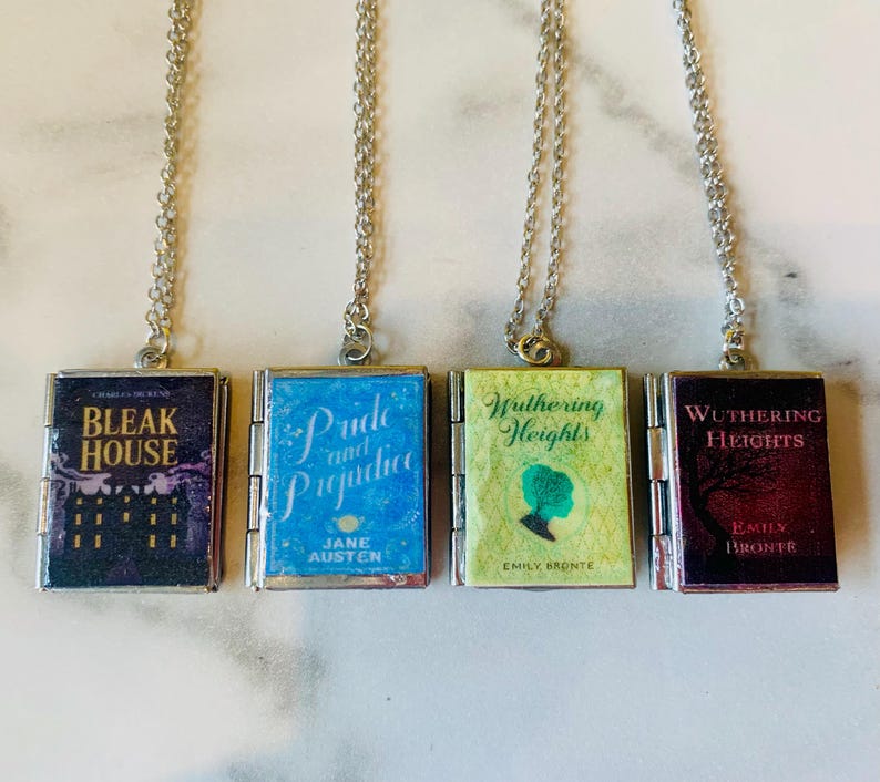 May include: Four silver-toned necklaces each feature a miniature book pendant. The book covers display titles like "Bleak House" and "Pride and Prejudice." The pendants are rectangular with a silver border and attached to a delicate chain.