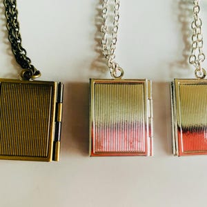 May include: Three rectangular locket necklaces with vertical ribbed detailing. One locket is bronze-toned with a dark chain, and the other two are silver-toned with silver chains. The lockets are hinged and appear to open.