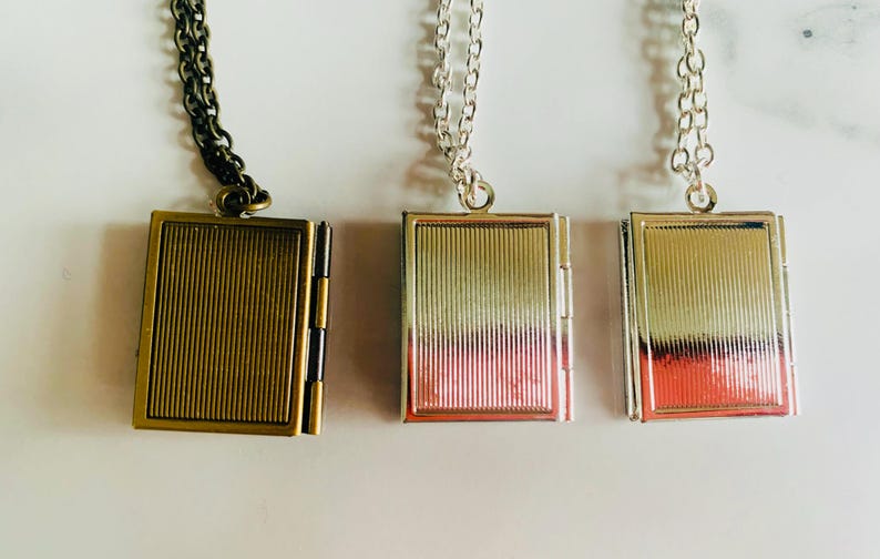 May include: Three rectangular locket necklaces with vertical ribbed detailing. One locket is bronze-toned with a dark chain, and the other two are silver-toned with silver chains. The lockets are hinged and appear to open.