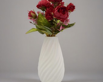 May include: A white ceramic vase with a swirling pattern, holding a bouquet of red and pink artificial flowers.