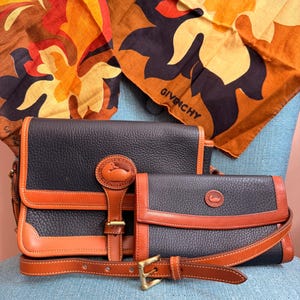 May include: Two vintage leather handbags in navy blue and tan with brass hardware. The bags have a pebbled texture and are accented with tan leather trim and straps. A patterned scarf with the Givenchy logo is in the background.