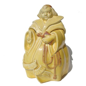 May include: A ceramic cookie jar in the shape of a monk, wearing a yellow robe and holding a book. The jar has a banner that reads "Thou Shalt Not Steal". The monk is making a hand gesture. The jar is a vintage item.