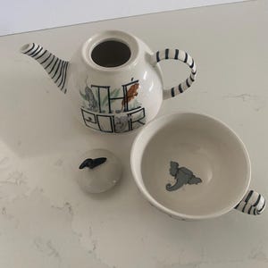 Puede incluir: Un juego de t&eacute; de cer&aacute;mica blanca con detalles de rayas negras. El juego incluye una tetera con el texto "THE POUR", una tapa y una taza de t&eacute;. La tetera y la taza presentan ilustraciones de animales.