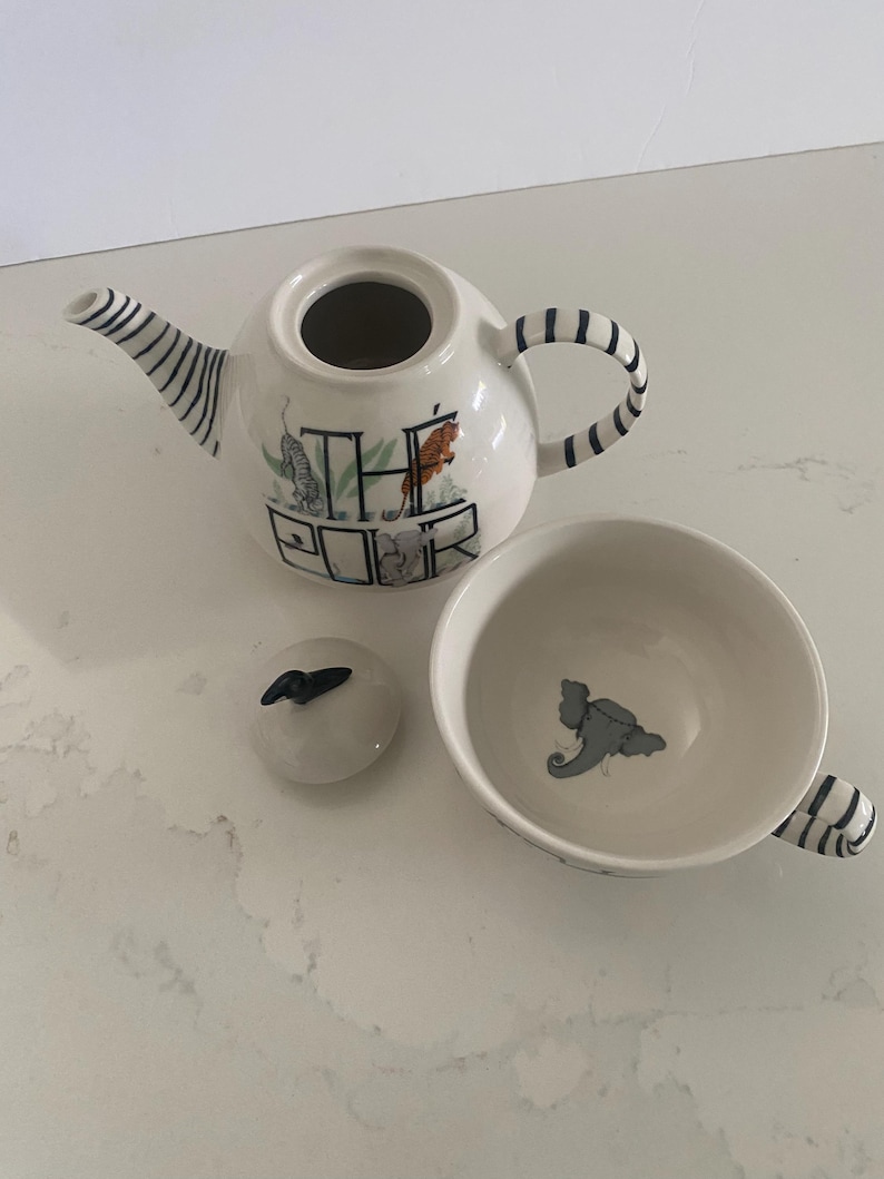 Puede incluir: Un juego de t&eacute; de cer&aacute;mica blanca con detalles de rayas negras. El juego incluye una tetera con el texto "THE POUR", una tapa y una taza de t&eacute;. La tetera y la taza presentan ilustraciones de animales.