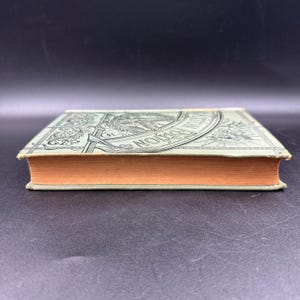 May include: An antique book with a light green cover and orange-colored pages. The cover features an ornate design with the words "Edition" and "Norton" visible. The book is closed and resting on a dark surface.