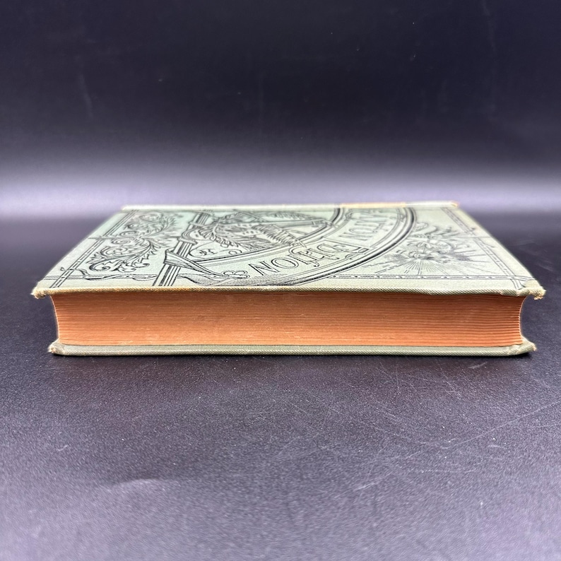 May include: An antique book with a light green cover and orange-colored pages. The cover features an ornate design with the words "Edition" and "Norton" visible. The book is closed and resting on a dark surface.