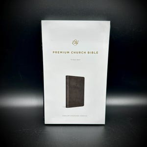 May include: A white package with gold text and a small image of a brown Bible. The text reads "PREMIUM CHURCH BIBLE" and "ENGLISH STANDARD VERSION". The Bible is a religious item.