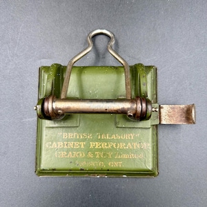 May include: An antique green "British Treasury" cabinet perforator with a metal handle and lever. The text "GRAND & TOY Limited, Toronto, ONT." is printed on the front in gold lettering. The perforator has a rectangular shape with rounded edges.
