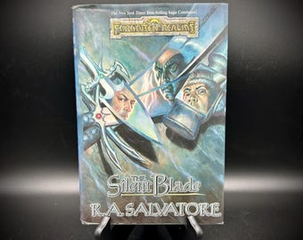 May include: A paperback book titled "The Silent Blade" by R.A. Salvatore. The cover features illustrations of three faces and a sword, with the text "Forgotten Realms" and "The New York Times Best-Selling Saga Continues!"