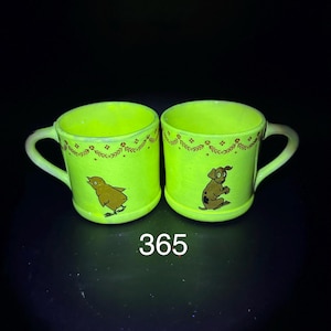 May include: Two neon green ceramic mugs with white handles. Each mug features a brown cartoon animal: a bird and a dog. A decorative brown floral pattern adorns the top rim of each mug. The number "365" is printed in white.