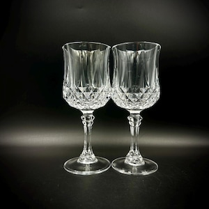 May include: Two clear crystal wine glasses with diamond-cut patterns on the bowl and a slender stem. The glasses have a tulip shape and sit on a round base. The background is black.