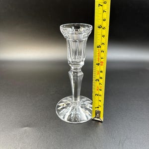 May include: A clear crystal candlestick holder with a starburst base and a fluted top. The candlestick is approximately 6 inches tall.
