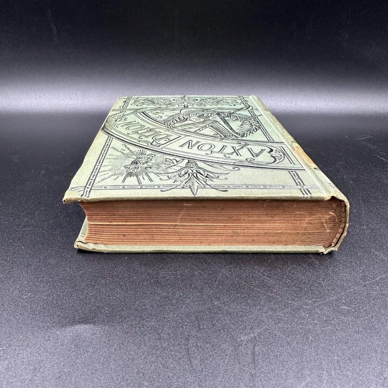 May include: An antique book with a light green cover featuring the text "Baxton's Dictionary" in a decorative font. The book's pages are aged, and the edges are worn, suggesting its age and use.