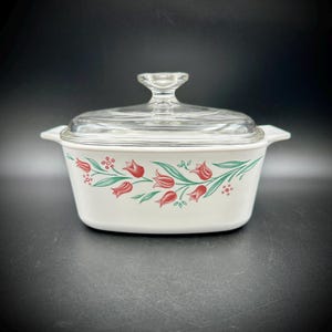 May include: White casserole dish with a clear glass lid. The dish features a floral pattern of red tulips and green leaves. The dish has two small handles on either side.