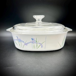 May include: White casserole dish with a clear glass lid. The dish features a floral design with blue irises and green leaves. The dish has a clear glass handle on the lid and two side handles.