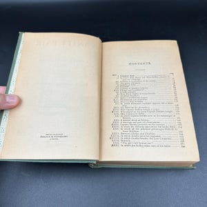 May include: An open book with aged, yellowed pages and a green cover. The book's contents are visible, with a detailed table of contents and text. The spine is visible, and the book is held open by a hand. The book is printed by Donohue & Henneberry, Chicago.