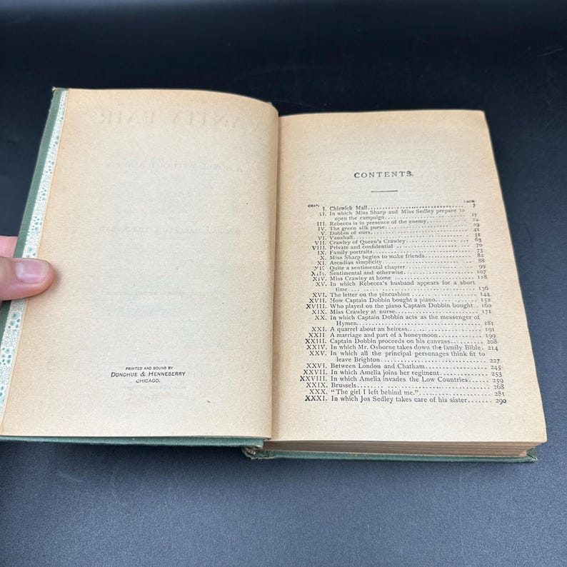May include: An open book with aged, yellowed pages and a green cover. The book's contents are visible, with a detailed table of contents and text. The spine is visible, and the book is held open by a hand. The book is printed by Donohue & Henneberry, Chicago.