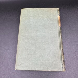 May include: A vintage book with a light green cover. The spine is decorated with ornate designs and a strip of tan paper. The book is closed and angled, showing the cover and spine against a dark background.