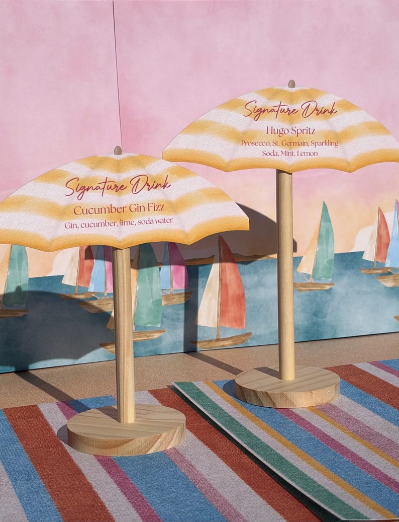 K&ouml;nnte beinhalten: Zwei Miniatur-Strandschirme aus Holz als Getr&auml;nkekarten. Der linke Schirm zeigt Signature Drink, Cucumber Gin Fizz, Gin, cucumber, lime, soda water. Der rechte zeigt Signature Drink, Hugo Spritz, Prosecco, St. Germain, Sparkling Soda, Mint, Lemon.