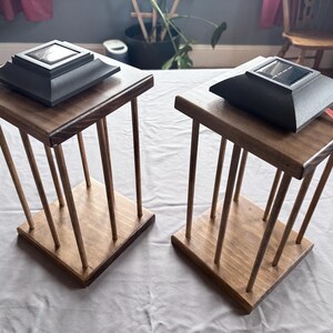May include: Two wooden side tables with solar lanterns. Each table features a square top and base, linked by vertical wooden rods. The lanterns are black with a square solar panel. Tables are on a white surface. The tables are approximately 40 cm tall.