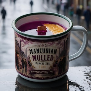 May include: A white enamel mug with a green rim containing a dark purple liquid, a wooden stirrer, and an orange slice. The mug features a label with the text "MANCUNIAN MULLED MANCHESTER 1908" and illustrations of people in a city setting.