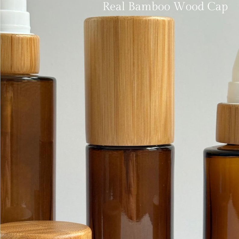 May include: Close-up of amber glass bottles with real bamboo wood caps. The bottles have a cylindrical shape and a spray nozzle. The text "Real Bamboo Wood Cap" is visible at the top of the image. The bottles are likely for essential oils or cosmetic products.