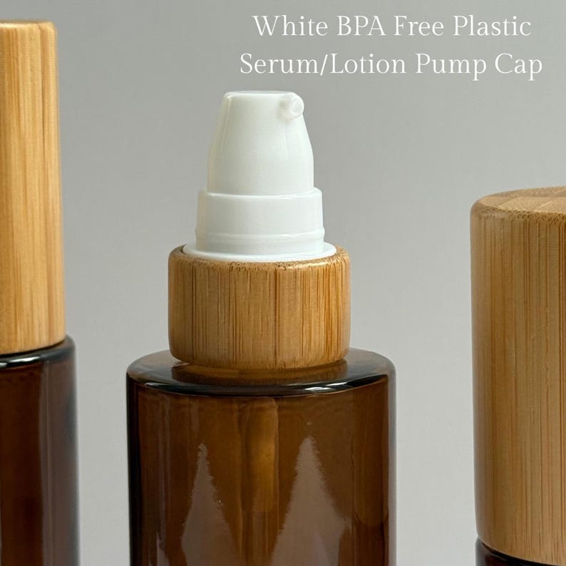 May include: Close-up of a brown glass bottle with a white serum/lotion pump cap and a bamboo-colored collar. The text "White BPA Free Plastic Serum/Lotion Pump Cap" is visible. The bottle is designed for skincare products.