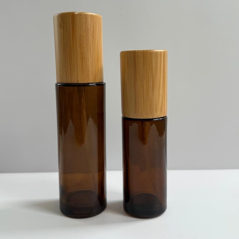 May include: Two brown glass spray bottles with natural bamboo lids. The bottles are different sizes, with one taller than the other. The bottles are empty and ready to be filled with essential oils, perfumes, or other liquids.