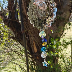 Peut inclure: Un mobile de vent en métal argenté représentant le soleil et la lune, avec un prisme de cristal suspendu. Le prisme est orné d'un charme en forme d'étoile à sa base et est composé de cristaux transparents, bleus et jaunes.