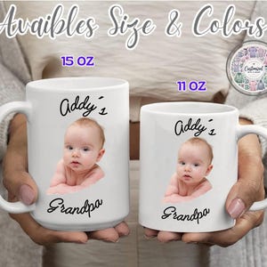 May include: Two white ceramic mugs, 15 oz and 11 oz, are held in hands. Each mug features a baby's photo, the name "Addy's", and the word "Grandpa" in black script. The text "Available Size & Colors" is at the top.