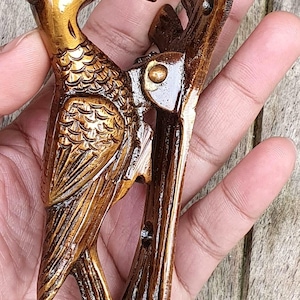 May include: A detailed, wooden bird sculpture with a long beak and textured feathers. The bird is perched on a branch-like structure, all finished in a warm, glossy brown. The sculpture is likely a decorative item.