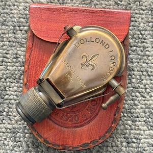 Peut inclure: Un monoculaire en laiton avec un oculaire texturé et un bouton de réglage latéral, portant l'inscription gravée DOLLOND LONDON, un symbole de fleur de lys et l'année 1920. Il repose sur un étui en cuir marron gaufré avec 1920 et une étoile.