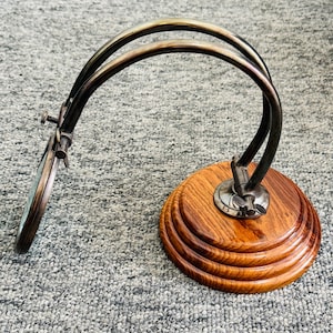 May include: A vintage magnifying glass with a wooden base and a curved metal frame. The magnifying glass is round and angled, with a dark metal finish. The base is made of polished wood.