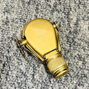 May include: A vintage brass monocular with a textured grip and hinged cover. The monocular is a warm gold colour and appears to be in good condition. The design suggests it may be a nautical or military item.