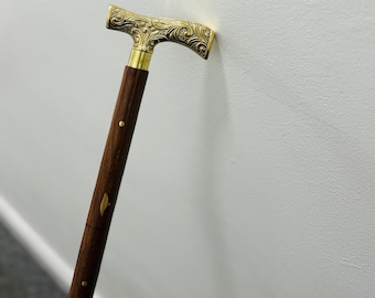 May include: A wooden walking cane with a gold-colored handle. The handle has an ornate, floral design. The shaft is dark brown with gold-colored accents.