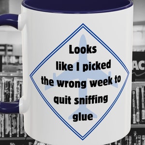 May include: White ceramic mug with a blue rim and handle. The mug has a blue and white diamond-shaped design with the text "Looks like I picked the wrong week to quit sniffing glue".