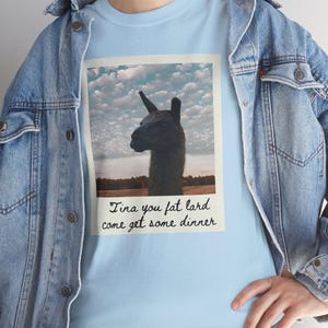 May include: A light blue t-shirt with a vintage-style photo of a llama. The photo has the text "Tina you fat lard come get some dinner" written below it.
