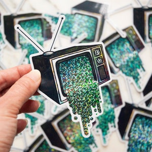 May include: A sticker of a vintage television with green glitter pouring out of the screen. The sticker is on a white background.
