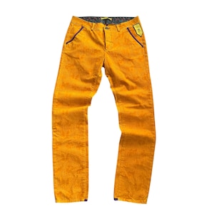 Op de afbeelding: Mosterdgele corduroy broek met een geometrisch patroon. De broek heeft paarse zakafwerking en een kleine patch op de rechterzak. De broek wordt op een witte achtergrond gepresenteerd.