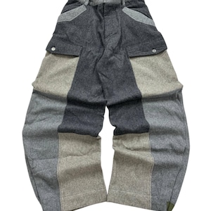 May include: Patchwork trousers in shades of grey and beige, featuring a button fastening and two cargo pockets. The design incorporates panels of varying grey and beige fabrics. The trousers are made of a soft material.