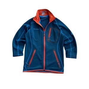 May include: A blue fleece jacket with orange detailing. The jacket has a full zip, several zipped pockets, and the brand name "MAMMUT" on the chest. The collar and pocket zips are orange, and the jacket has blue trim.