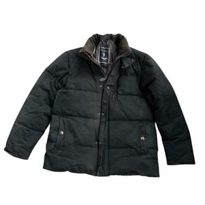 May include: A black quilted jacket with a brown corduroy collar. The jacket features a button-up front, two side pockets, and a plaid lining visible at the collar. The jacket is a medium weight and appears to be made of a durable material.