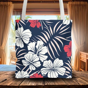 May include: A navy blue tote bag with a floral pattern. The design features large white hibiscus flowers, red hibiscus flowers, and light pink palm leaves. The bag has white straps and is made of a sturdy fabric.